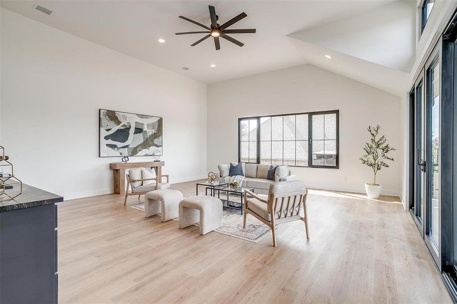 Living area featuring visible vents, baseboards, high vaulted ceiling, ceiling fan, and light wood-style floors