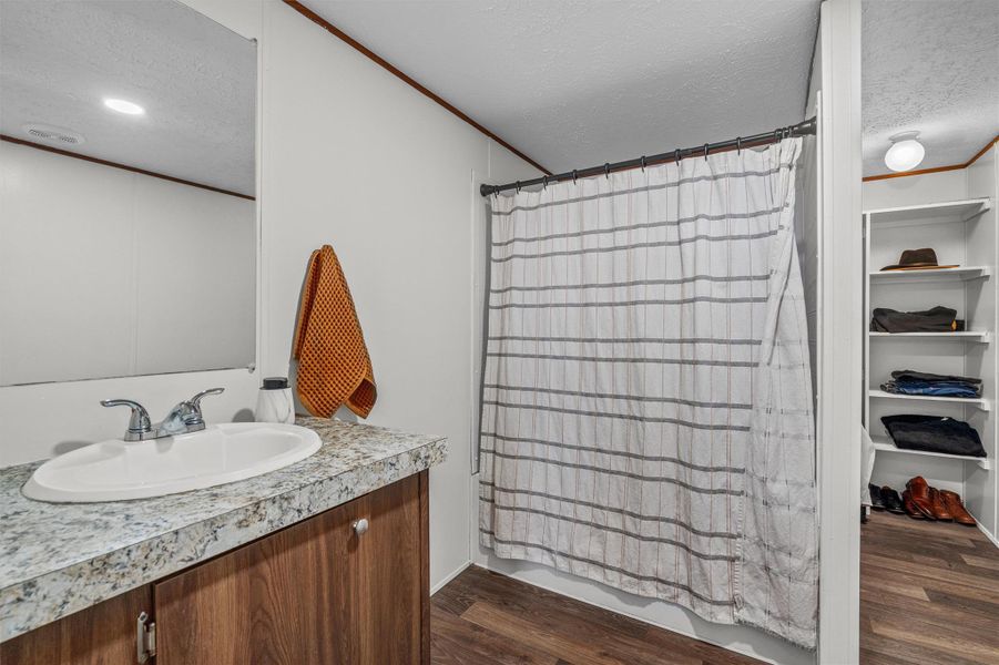 Full bathroom with a textured ceiling, ornamental molding, vanity, dark wood-style floors, and a closet
