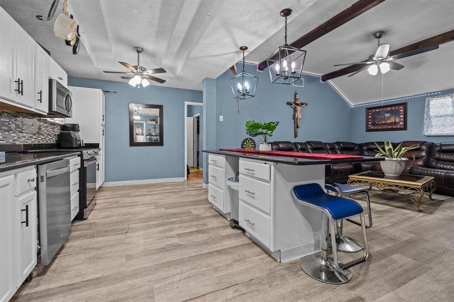 Kitchen featuring hanging light fixtures, appliances with stainless steel finishes, a kitchen breakfast bar, and white cabinetry