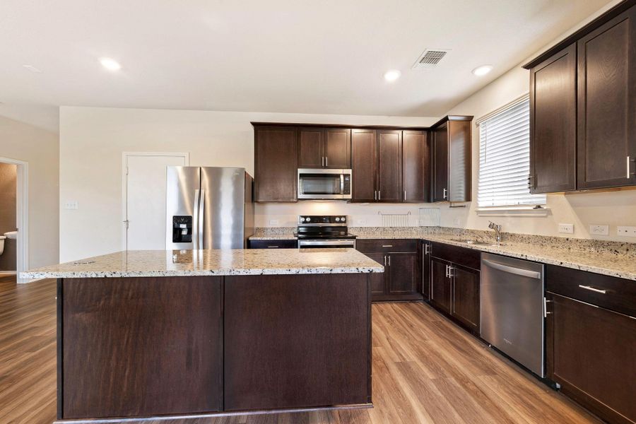 A well-appointed kitchen showcasing dark wood cabinetry, gleaming stainless steel appliances, and a generously sized island. A well-appointed kitchen showcasing dark wood cabinetry, gleaming stainless steel appliances, and a generously sized island.
