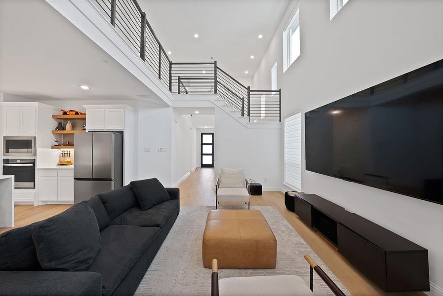Open-concept living area with a double-height ceiling, light wood-finish flooring, and a modern stair railing