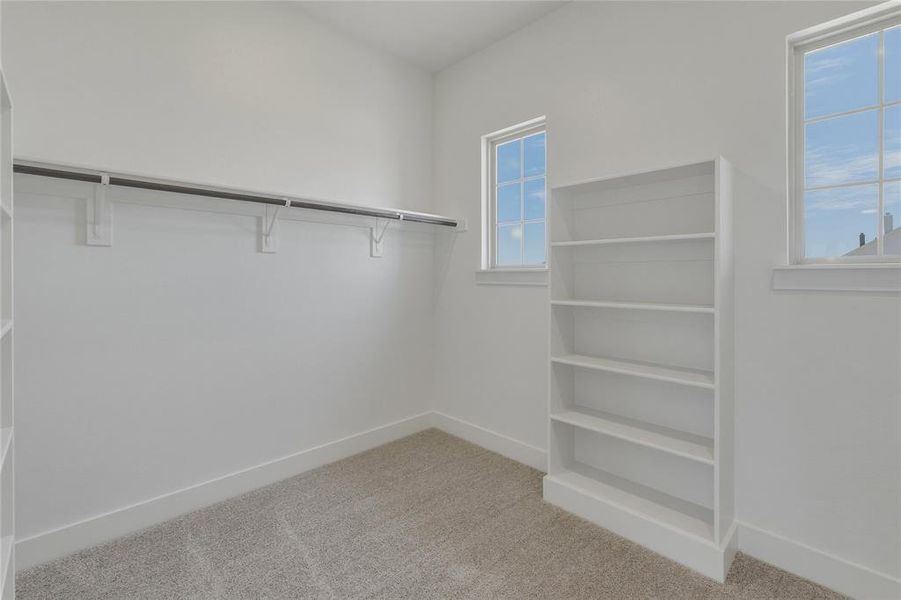 Carpeted room with a built-in five-shelf bookcase, two single-hung windows, and a full-length clothes rod with shelving Carpeted room with a built-in five-shelf bookcase, two single-hung windows, and a full-length clothes rod with shelving