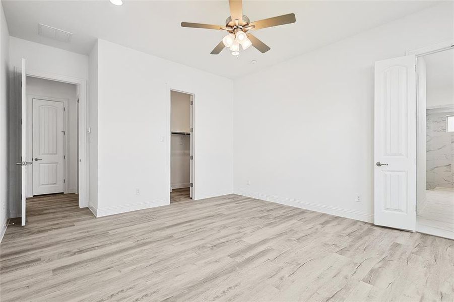 Unfurnished bedroom featuring ceiling fan, a walk in closet, a closet, light hardwood / wood-style floors, and connected bathroom