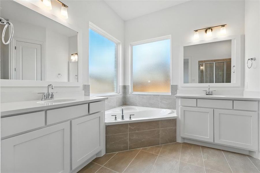 Full bathroom with light tile patterned floors, a stall shower, a garden tub, and two vanities