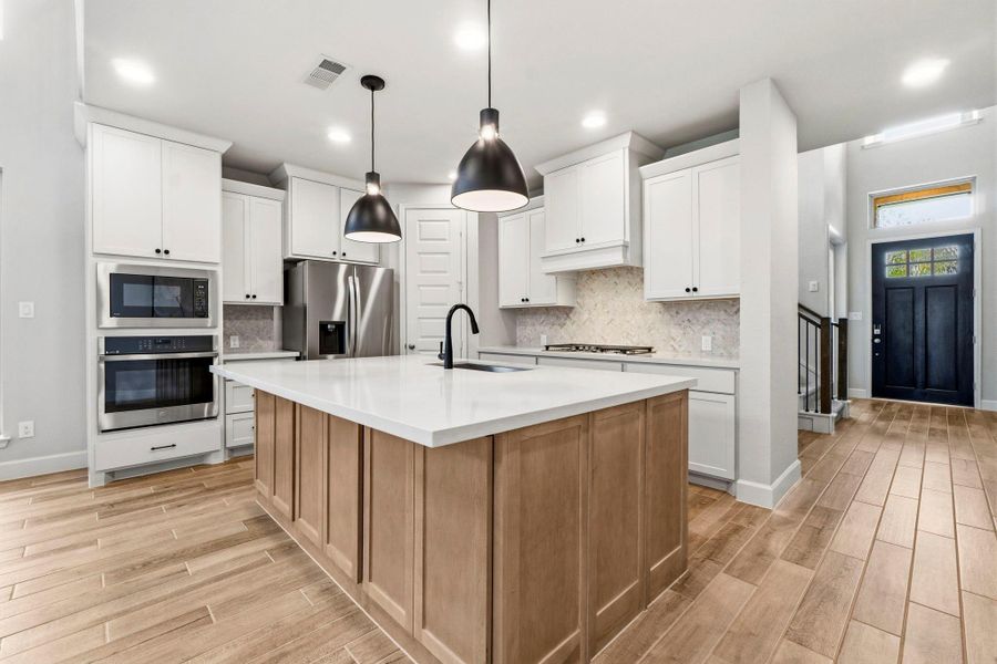 The beautifully designed kitchen features elegant quartz countertops, a designer tile backsplash, 5-Burner gas stovetop, stylish pendant lighting, an oversized island with abundant storage, and ample cabinetry to keep everything organized.
