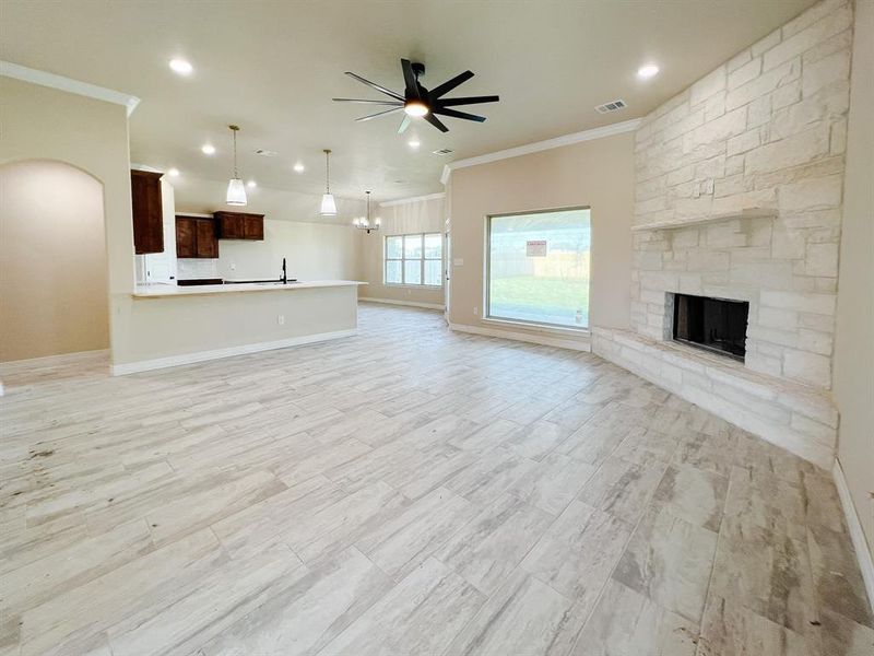 Unfurnished living room with crown molding, light wood-style flooring, a fireplace, arched walkways, and a chandelier Unfurnished living room with crown molding, light wood-style flooring, a fireplace, arched walkways, and a chandelier