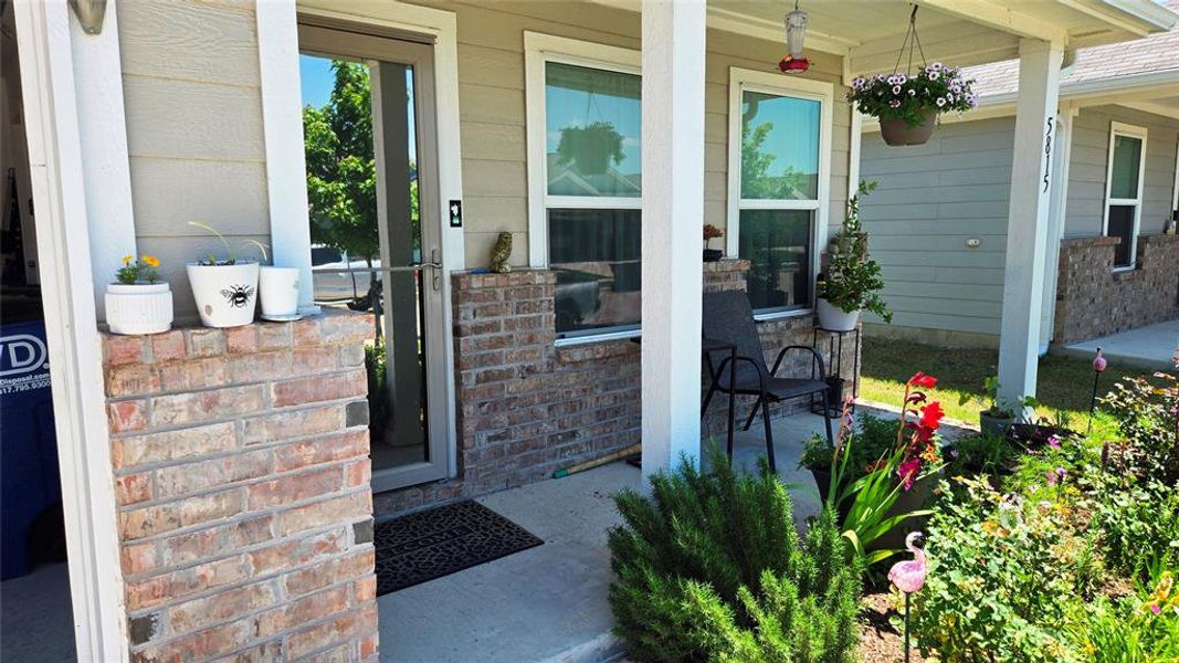 Covered front porch featuring brick accents, light-colored siding, and white trim