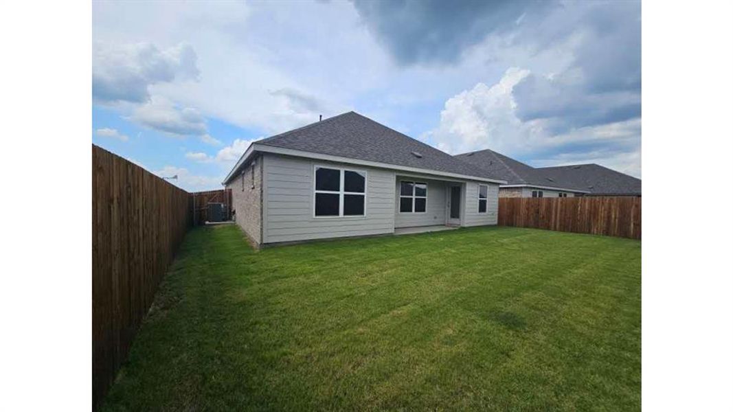 Expansive backyard featuring a manicured lawn, full wood privacy fencing, and a covered concrete patio