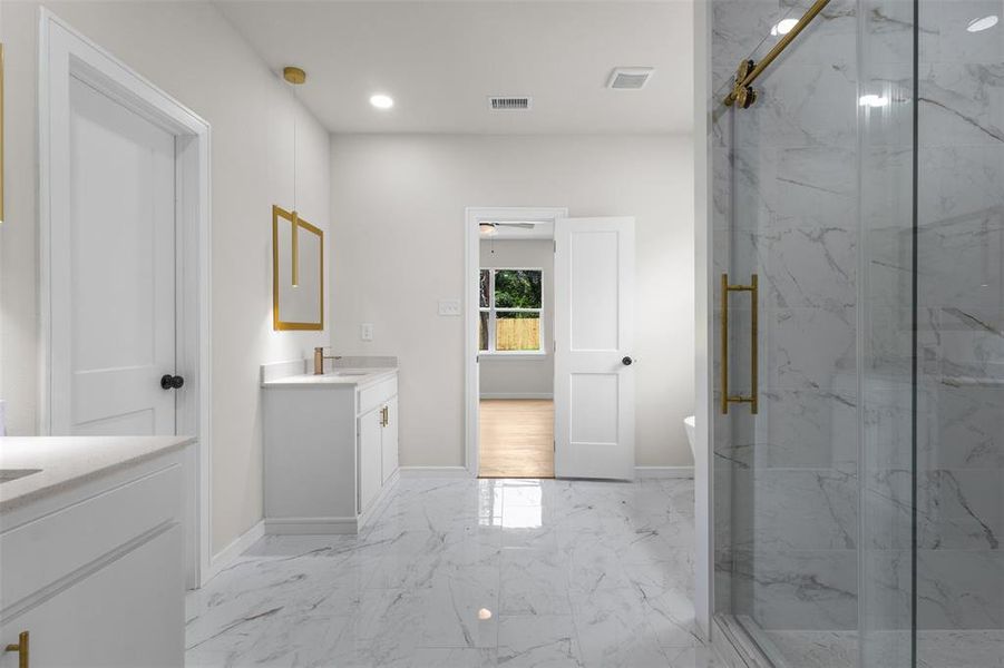 Spacious bathroom featuring marble-look tile flooring, a glass-enclosed shower with gold-tone hardware, and dual white vanity cabinets with integrated sinks and gold-tone fixtures