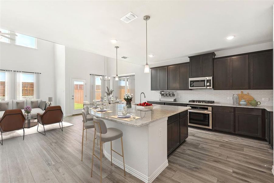 Kitchen with hanging light fixtures, light stone countertops, a kitchen island with sink, light hardwood / wood-style floors, and stainless steel appliances