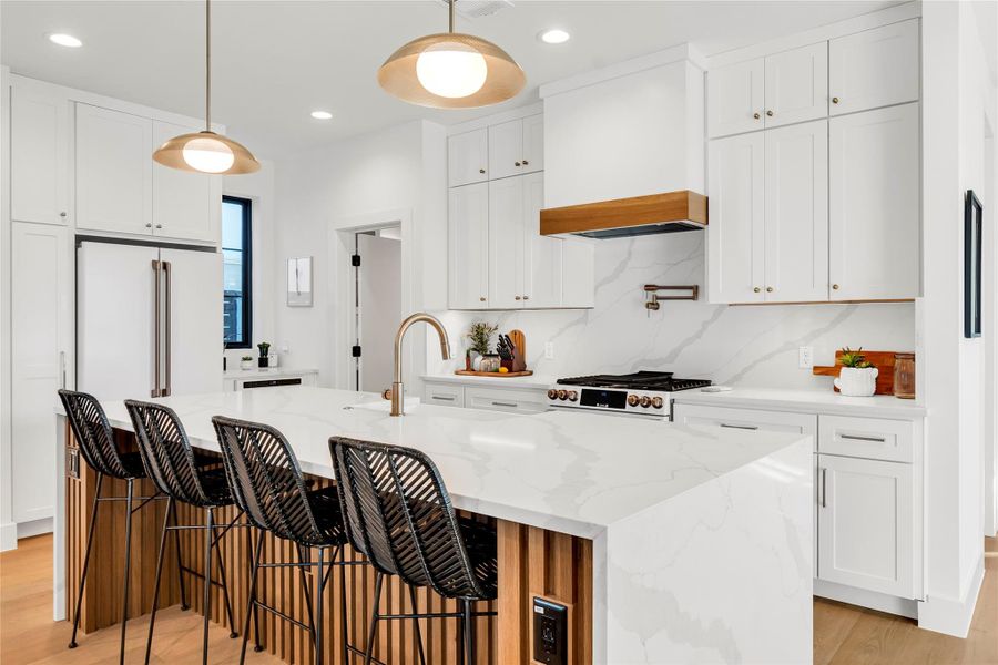 Kitchen with white cabinetry, light wood-style floors, backsplash, light stone countertops, and a breakfast bar area Kitchen with white cabinetry, light wood-style floors, backsplash, light stone countertops, and a breakfast bar area
