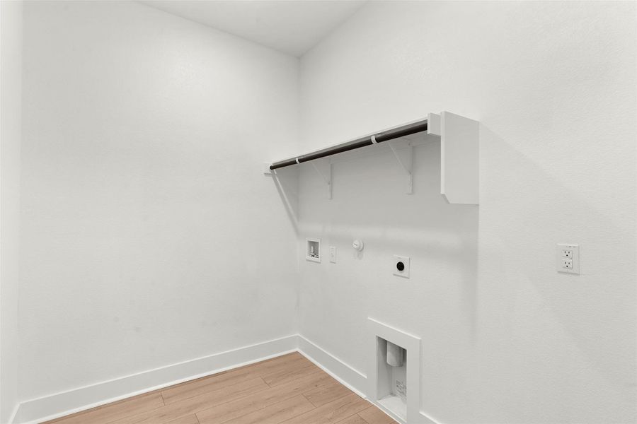 Laundry area featuring wood-finish flooring, white walls, and a built-in clothes rod with shelving Laundry area featuring wood-finish flooring, white walls, and a built-in clothes rod with shelving
