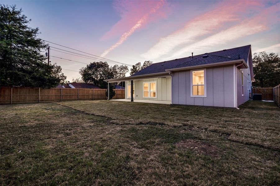 Back house at dusk with a yard and a patio