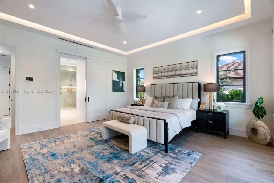 Tray ceiling with recessed lighting, porcelain-finish flooring, sliding interior door, and multi-pane windows with dark framing Tray ceiling with recessed lighting, porcelain-finish flooring, sliding interior door, and multi-pane windows with dark framing