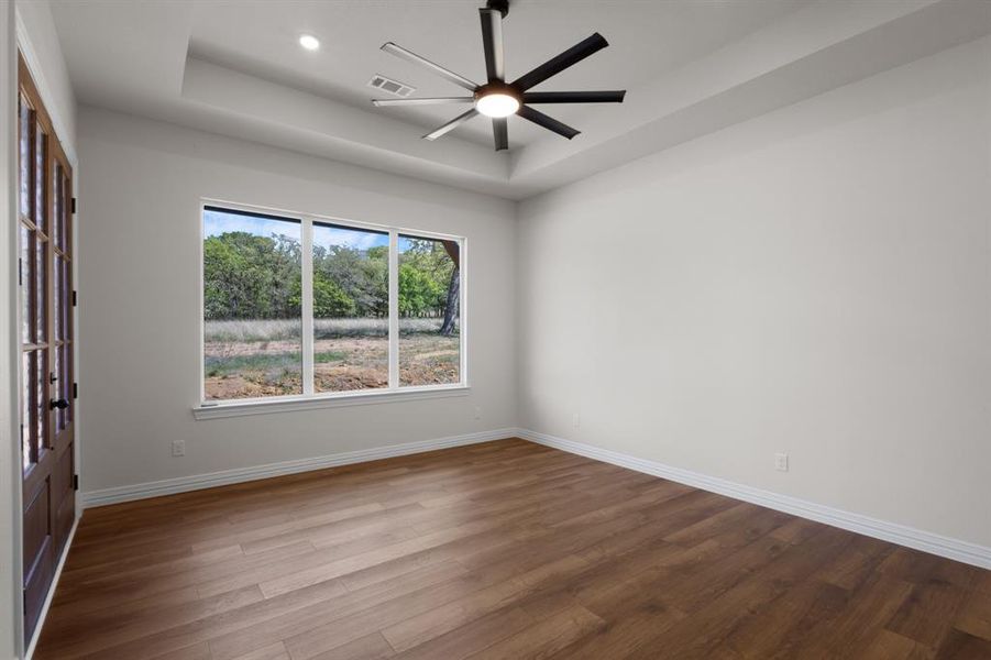 Spare room with ceiling fan, a tray ceiling, visible vents, baseboards, and dark wood-style floors