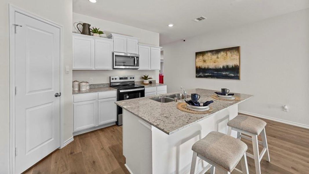 Kitchen featuring white cabinets, stainless steel appliances, a breakfast bar area, dark wood-style flooring, and a center island with sink