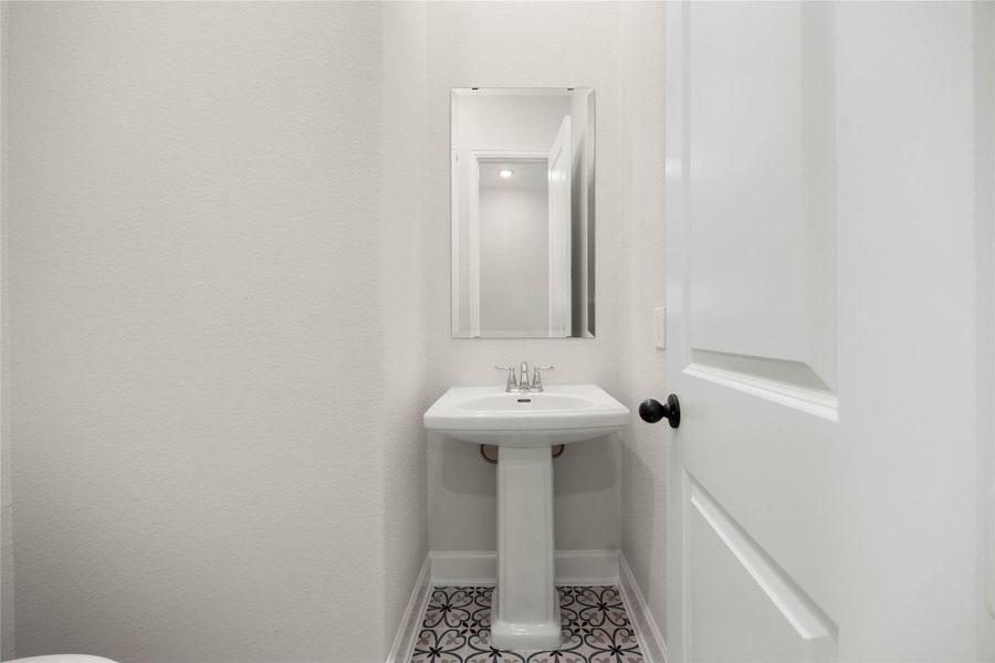Charming first-floor powder bath perfectly situated for guests and daily convenience. This beautifully appointed half-bath features a classic white porcelain pedestal sink with polished chrome fixtures and a sleek, frameless vertical vanity mirror. A striking highlight of the space is the custom patterned cement-look floor tile, adding a sophisticated pop of designer style to the clean, neutral color palette. Charming first-floor powder bath perfectly situated for guests and daily convenience. This beautifully appointed half-bath features a classic white porcelain pedestal sink with polished chrome fixtures and a sleek, frameless vertical vanity mirror. A striking highlight of the space is the custom patterned cement-look floor tile, adding a sophisticated pop of designer style to the clean, neutral color palette.