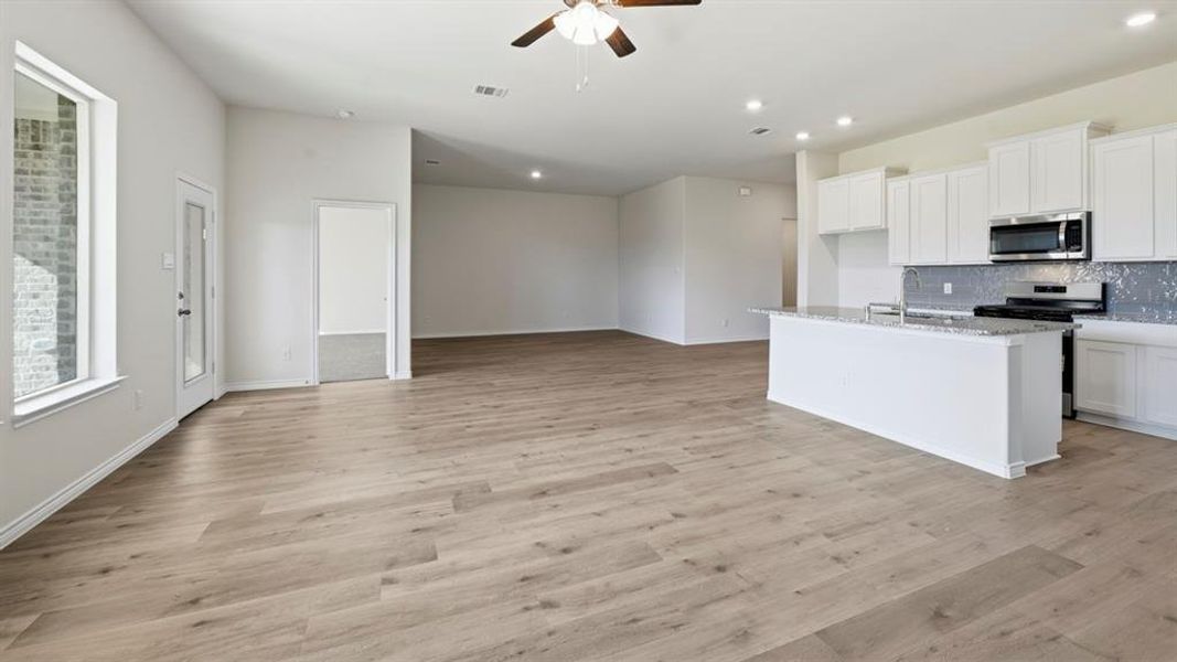 Kitchen with white cabinetry, stainless steel appliances, an island with sink, a ceiling fan, and light stone counters