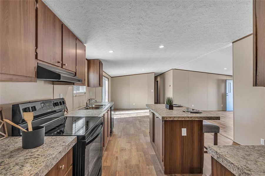 Kitchen featuring a textured ceiling, light hardwood / wood-style flooring, a kitchen bar, black electric range, and sink