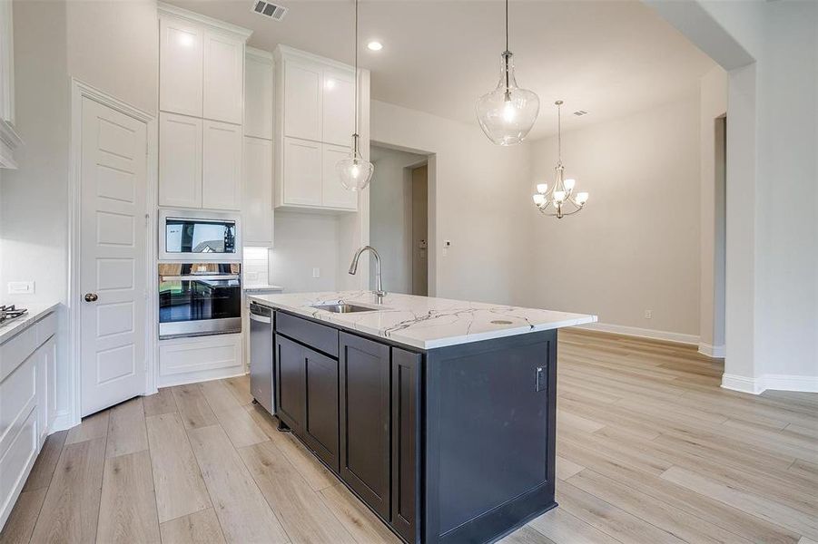 Kitchen with light stone countertops, stainless steel appliances, sink, a center island with sink, and white cabinets