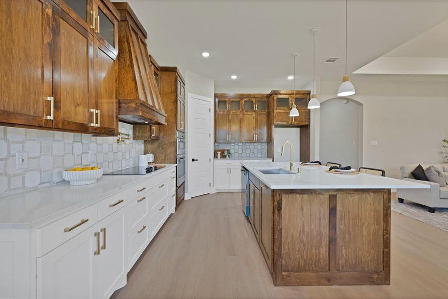 Kitchen with a sink, stainless steel appliances, glass insert cabinets, light wood-type flooring, and tasteful backsplash