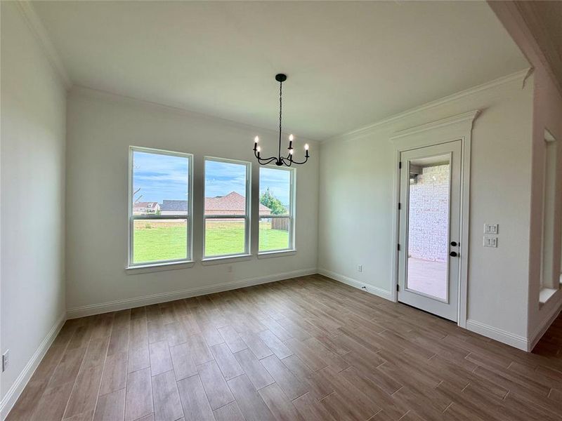 Spacious interior featuring wood-look tile flooring, crown molding, a black iron chandelier, and three large windows