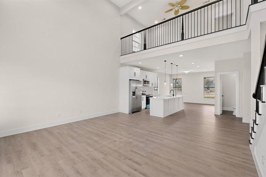Living room with recessed lighting, ceiling fan, light wood-style floors, and a high ceiling Living room with recessed lighting, ceiling fan, light wood-style floors, and a high ceiling