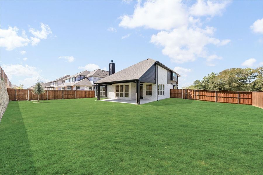 Backyard of two-story home with large green lawn, covered patio, and wood privacy fence Backyard of two-story home with large green lawn, covered patio, and wood privacy fence