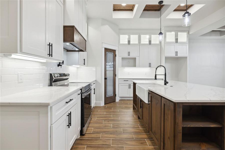 Kitchen with decorative light fixtures, white cabinetry, sink, a center island with sink, and electric stove