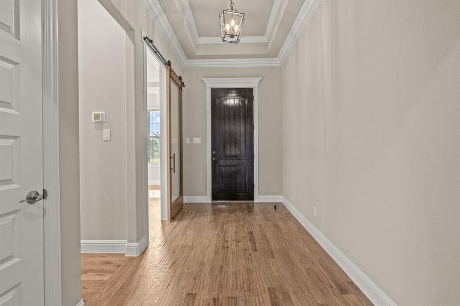 Entrance foyer with light wood-style floors, a raised ceiling, a barn door, and ornamental molding
