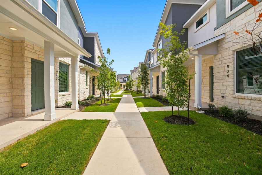 Concrete walkways trace through manicured green lawns bordered by stone-claddings and modern architectural facades.