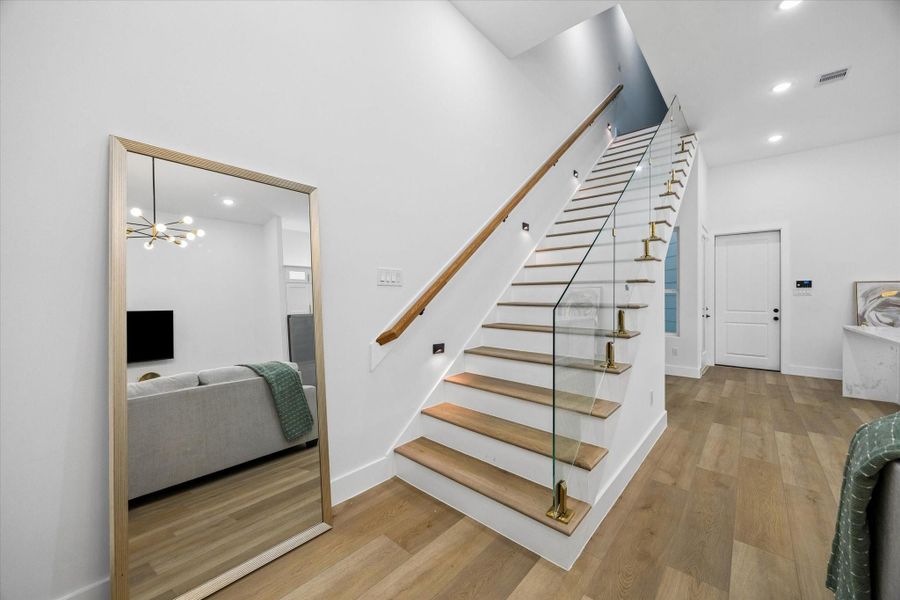 This photo showcases a modern, bright entryway featuring a wooden staircase with glass railing. The space is accented by a large mirror and sleek lighting, offering a stylish, open feel. This photo showcases a modern, bright entryway featuring a wooden staircase with glass railing. The space is accented by a large mirror and sleek lighting, offering a stylish, open feel.