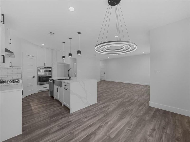 Kitchen featuring open floor plan, light stone countertops, backsplash, dark wood-type flooring, and hanging light fixtures Kitchen featuring open floor plan, light stone countertops, backsplash, dark wood-type flooring, and hanging light fixtures