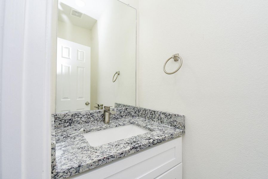 A modern bathroom vanity with granite countertop, inset sink, faucet, and a mounted mirror reflecting a white door.