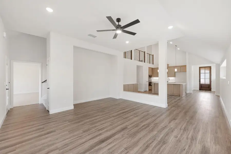 Open living area with wood-look floors, ceiling fan, and open view to kitchen with island
