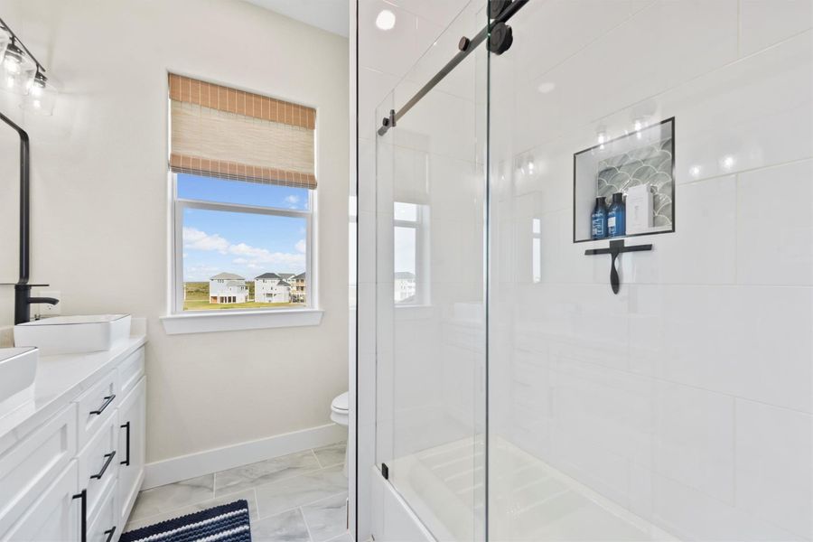 Bright, modern bathroom featuring a large glass-roller shower door, sleek white vanity with dual sinks, and a window with a scenic view.