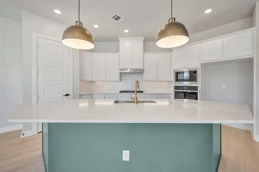 Kitchen with backsplash, light wood-type flooring, a kitchen island with sink, stainless steel appliances, and dual tone cabinets Kitchen with backsplash, light wood-type flooring, a kitchen island with sink, stainless steel appliances, and dual tone cabinets