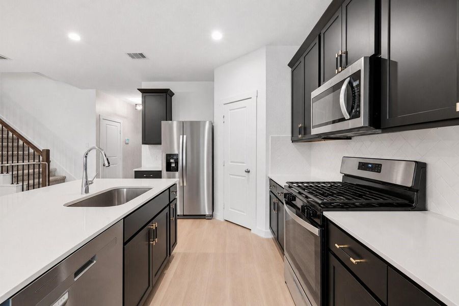 From this angle, the kitchen flows effortlessly into the entry hallway, highlighted by a spacious island, elegant dark cabinetry, and a thoughtfully designed, cohesive layout.