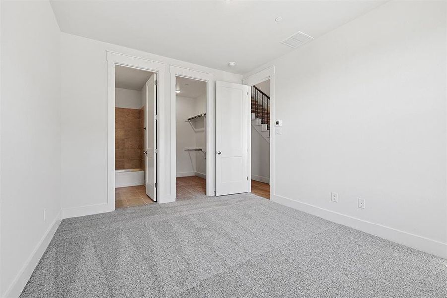 Unfurnished bedroom featuring a closet, light colored carpet, connected bathroom, and a walk in closet Unfurnished bedroom featuring a closet, light colored carpet, connected bathroom, and a walk in closet
