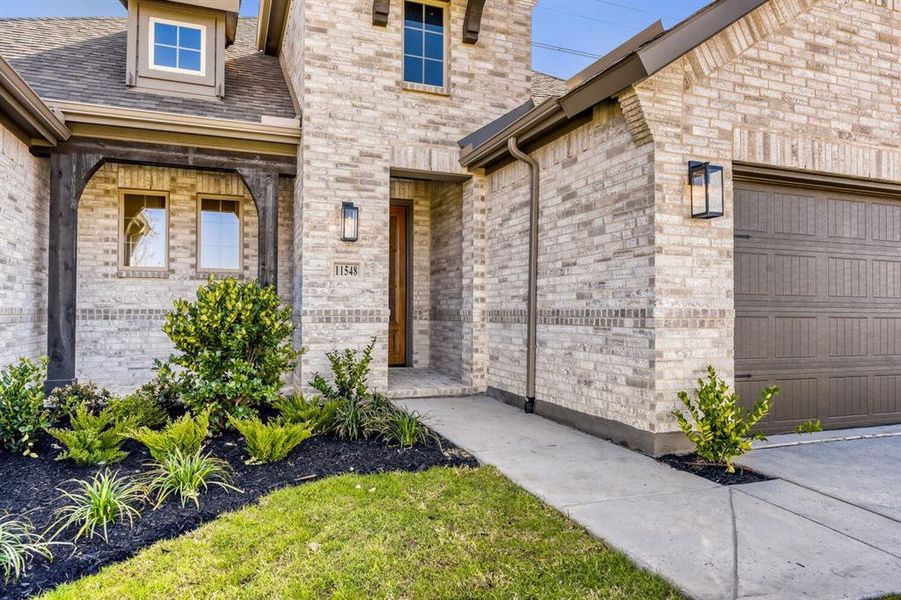 Doorway to property with a garage, brick siding, and a shingled roof