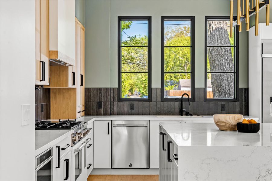 Kitchen with white cabinetry, light stone counters, stainless steel appliances, tasteful backsplash, and light wood finished floors