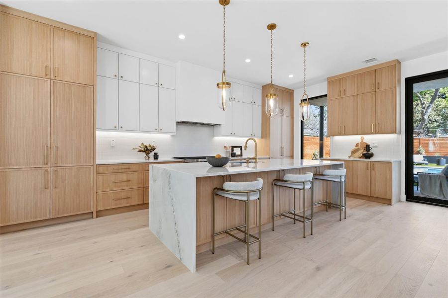 Dual tone kitchen featuring a kitchen breakfast bar, a large island with sink, light wood-style flooring, pendant lighting, and dual tone cabinets