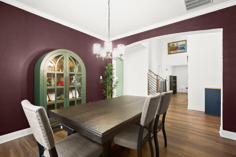 Dining area with arched walkways, ornamental molding, dark wood-style floors, a chandelier, and stairway Dining area with arched walkways, ornamental molding, dark wood-style floors, a chandelier, and stairway