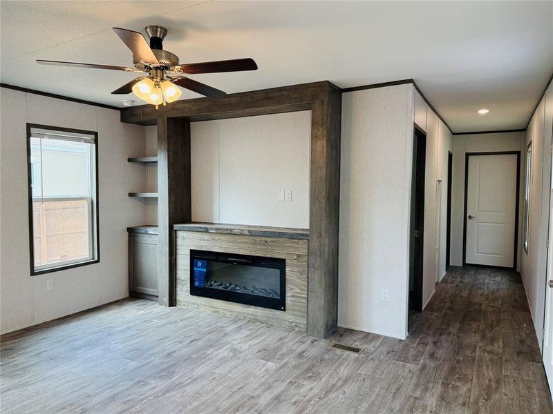 Unfurnished living room featuring wood finished floors, a glass covered fireplace, and a ceiling fan