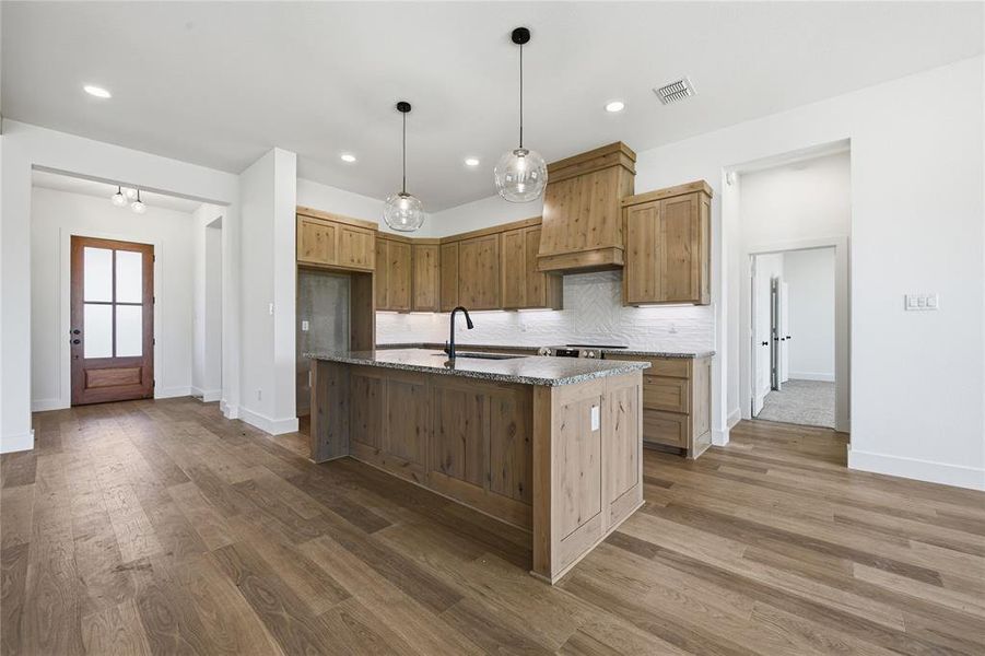 Kitchen with a kitchen island with sink, dark stone counters, dark wood-type flooring, and hanging light fixtures Kitchen with a kitchen island with sink, dark stone counters, dark wood-type flooring, and hanging light fixtures