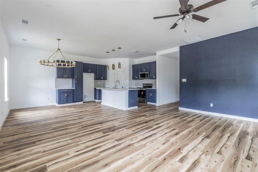 Unfurnished living room with light wood-style flooring, a sink, baseboards, ceiling fan, and a chandelier Unfurnished living room with light wood-style flooring, a sink, baseboards, ceiling fan, and a chandelier