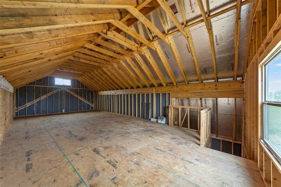 Unfinished bonus room featuring exposed wood framing, a wide window, and a smaller dormer window