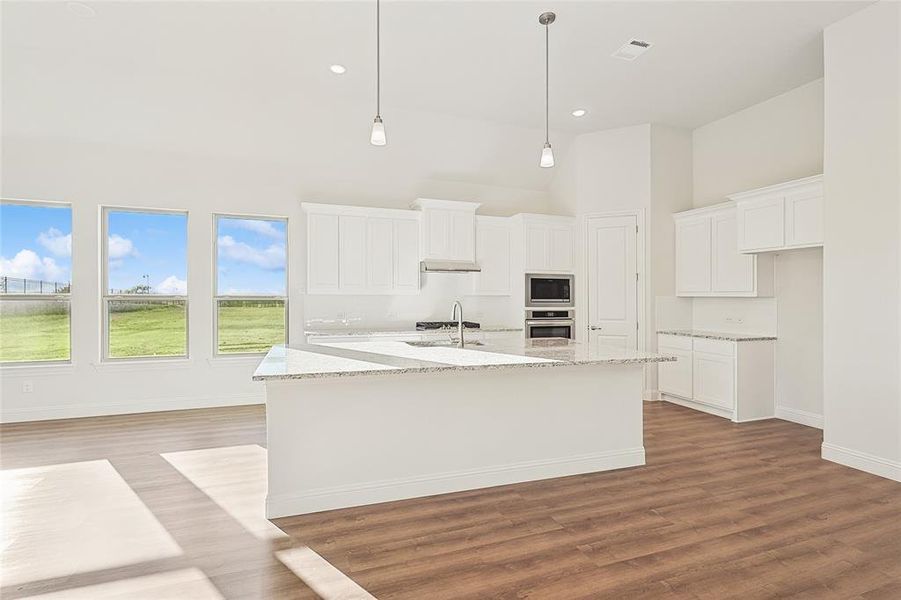 Kitchen featuring a center island with sink, light wood-style floors, a fireplace, light stone countertops, and white cabinetry Kitchen featuring a center island with sink, light wood-style floors, a fireplace, light stone countertops, and white cabinetry