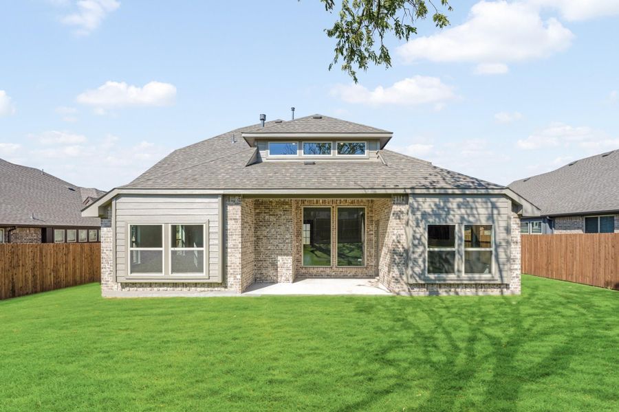 Rear exterior of brick home with covered patio, large windows, and fenced backyard with green lawn Rear exterior of brick home with covered patio, large windows, and fenced backyard with green lawn