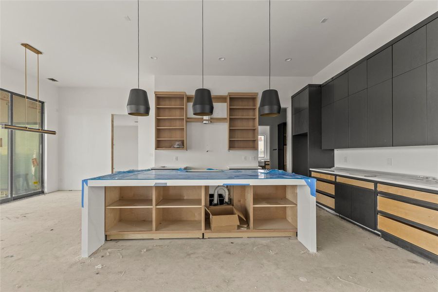 Kitchen featuring a central island with open shelving, matte black pendant lighting, dark cabinetry, and white countertops